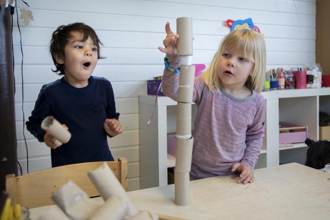En liten gutt og en liten jente som bygger tårn av dopapirruller