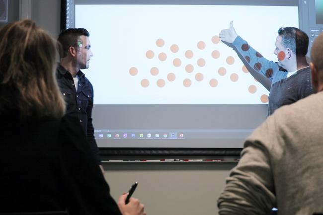 Illustrasjonsbilde av voksne som peker på noen prikker på et smartboard