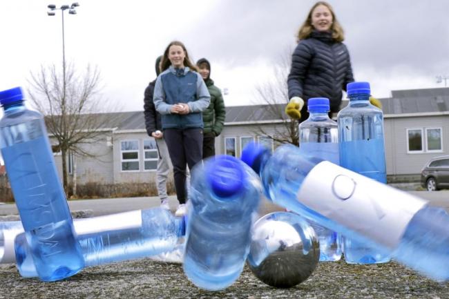 Elever som kaster en metallkule på plastikkflasker utendørs