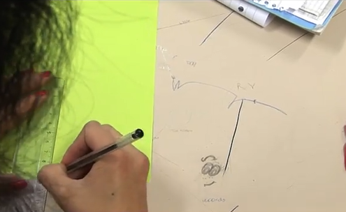 Elev som tegner en strek på et gult ark ved hjelp av en linjal. 